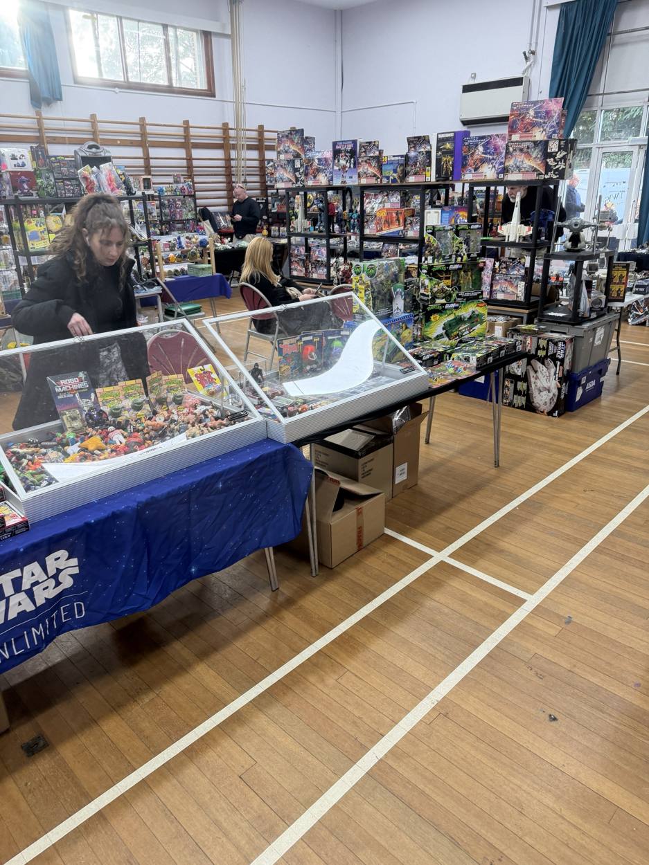 Visitors browsing glass display cases of loose figures in front of shelves of boxed Transformers